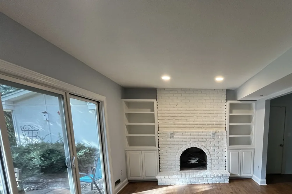 Freshly painted living room with a white-painted brick fireplace and built-in shelving by Smooth Painting